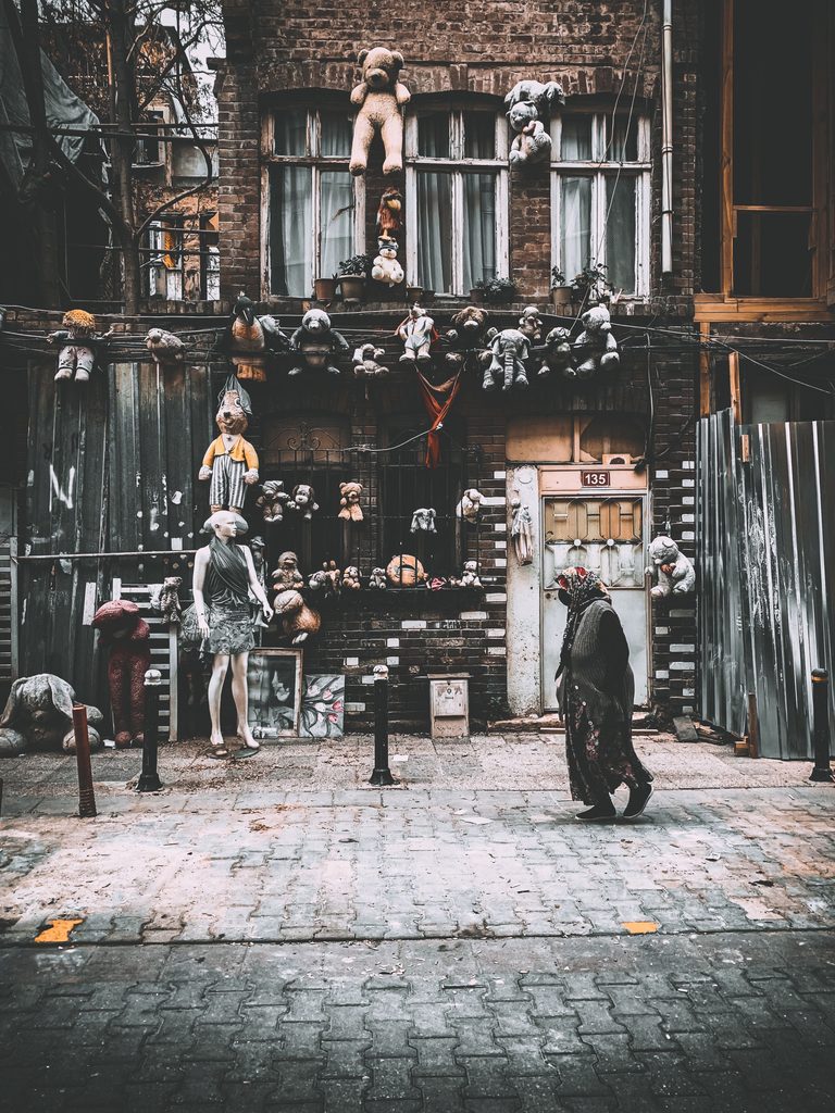 A cloaked figure walking past a storefront with old, weird toys hanging outside of it.